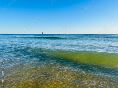 Small sail boat silhouette at the sea horizon, pure blue sky, deep blue sea