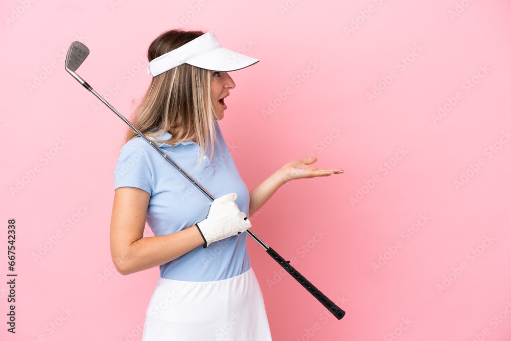 Young golfer player woman isolated on pink background with surprise expression while looking side Young golfer player woman isolated on pink background with surprise expression while looking side