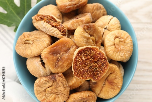 Bowl with tasty dried figs and green leaf on white wooden table, top view