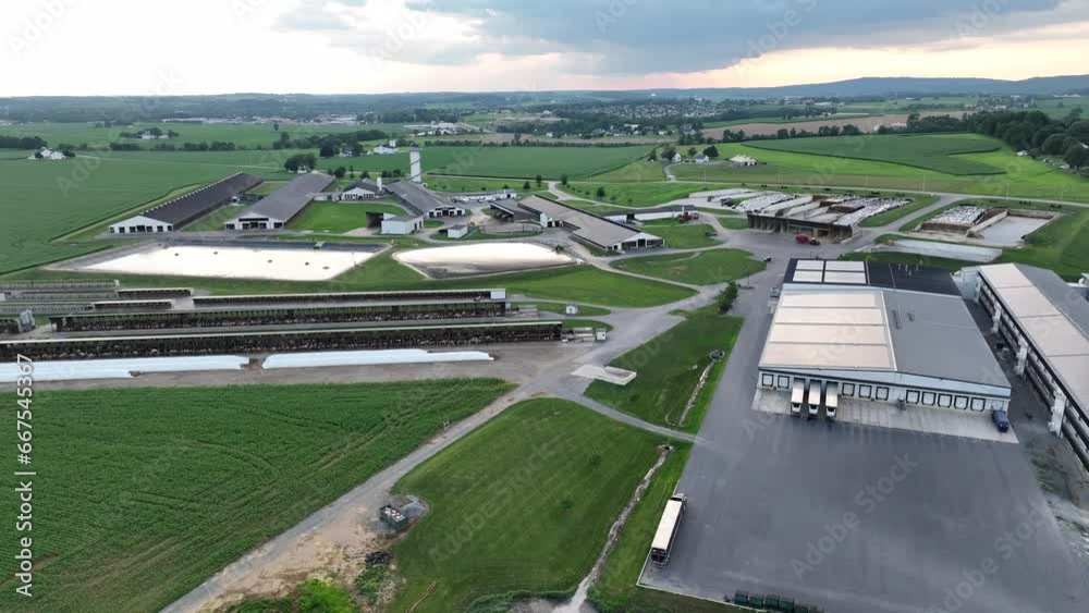 Expansive aerial shot capturing an industrial farm, with multiple sheds, storage facilities, and vast surrounding green fields, under a cloudy sky in USA. Aerial pull back reveal. Expansive aerial shot capturing an industrial farm, with multiple sheds, storage facilities, and vast surrounding green fields, under a cloudy sky in USA. Aerial pull back reveal.