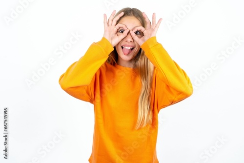 Beautiful teen girl doing ok gesture like binoculars sticking tongue out, eyes looking through fingers. Crazy expression.