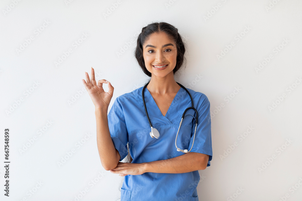 Portrait of happy young indian doctor woman in uniform showing okay gesture Portrait of happy young indian doctor woman in uniform showing okay gesture