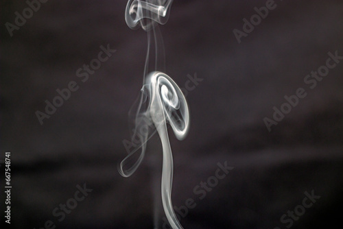Bizarre beautiful forms of white smoke from incense fly and swirl in the air on a dark background in a close-up 