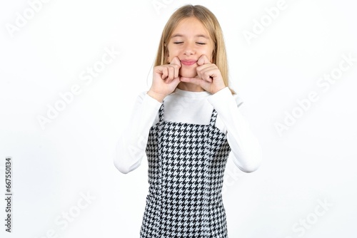 Pleased Beautiful teen girl with closed eyes keeps hands near cheeks and smiles tenderly imagines something very pleasant