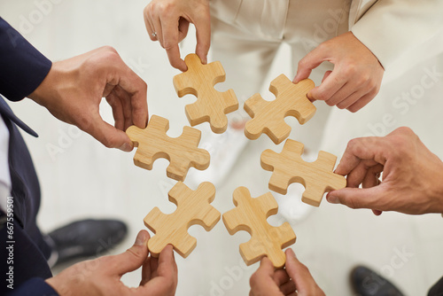 Top view cropped hands of a group of business people assembling wooden puzzle. Coworkers join jigsaw pieces in the office finding solution, working on project together. Support in teamwork concept.
