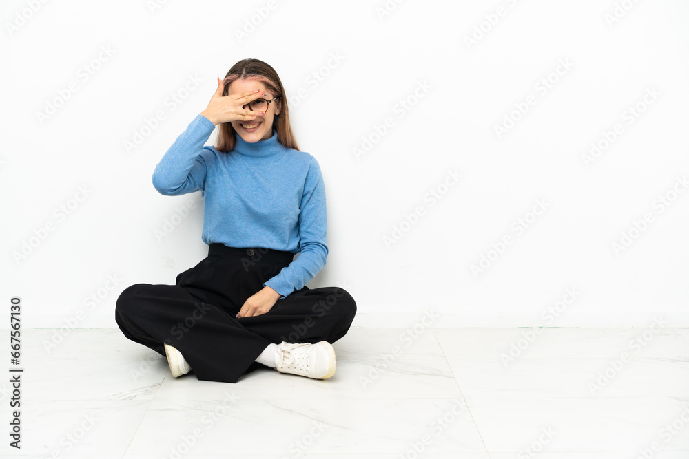 Young Caucasian woman sitting on the floor covering eyes by hands and smiling Young Caucasian woman sitting on the floor covering eyes by hands and smiling