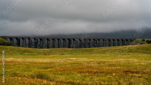 Scenic view of a railway bridge on a cloudy day, with grassy landscape in the foreground