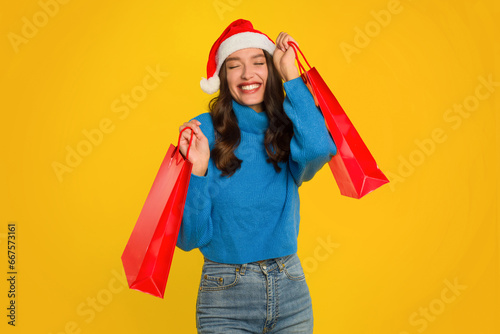 Happy woman in Santa hat holding shopping bags, yellow background