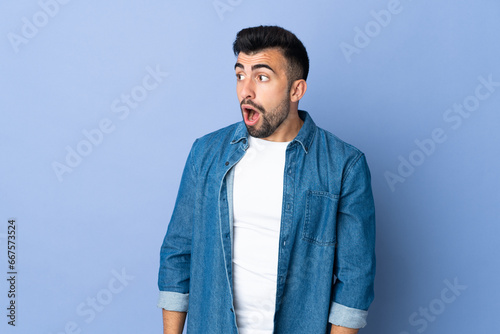 Caucasian man over isolated blue background doing surprise gesture while looking to the side