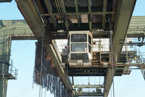 White cabin of green gantry crane operated by stevedores in Houston container terminal. There is upper part of construction of machinery and various cables. photo