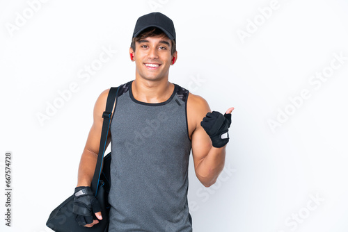 Young sport caucasian man with sport bag isolated on white background pointing to the side to present a product