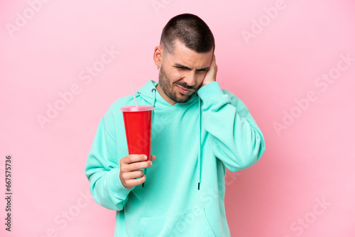 Young caucasian man holding soda isolated on pink background frustrated and covering ears