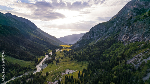 Beautiful sunset with a view of the green gorge and the river. coniferous trees, forests, lots of grass are all around. A seething gray river. Clouds in the sky. The rays of the sun. Steep cliffs