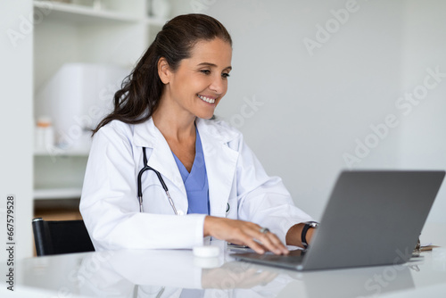 Mature doctor using laptop at clinic, telemedicine concept