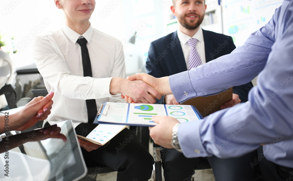 Close-up of smart colleagues smiling and shaking hand with prudent boss. Young manager giving important business project that determine future of corporation. Company meeting concept Close-up of smart colleagues smiling and shaking hand with prudent boss. Young manager giving important business project that determine future of corporation. Company meeting concept