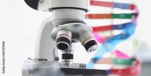 Microscope standing near multicolored model of dna chain in lab. Screening for hereditary genetic diseases concept