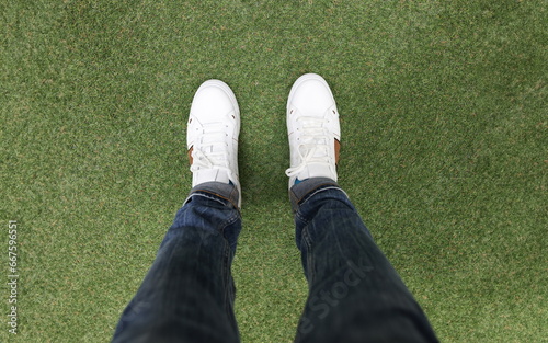 Male feet in white sneakers standing on green grass closeup. Walking in comfortable shoes concept