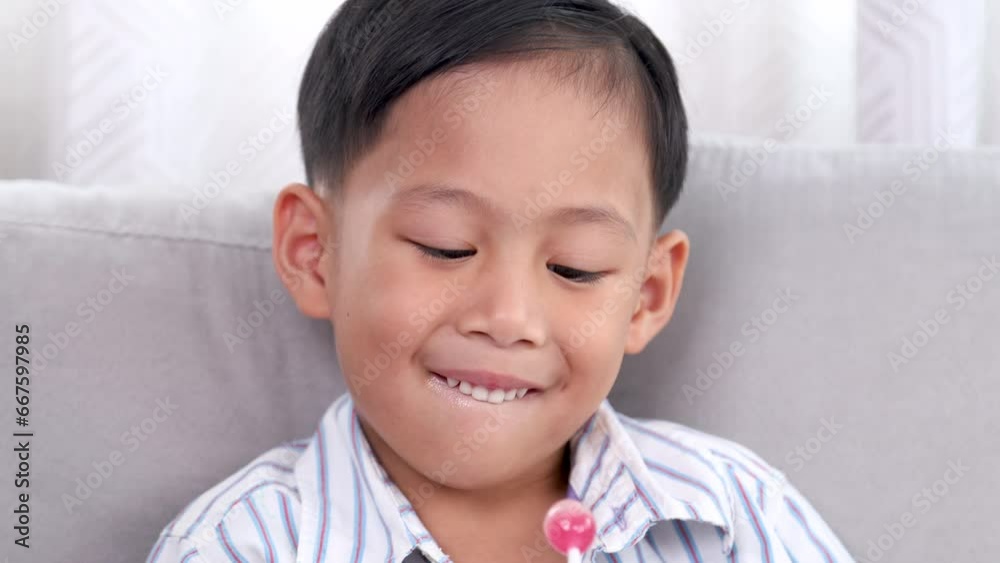 Close-up Asian little preschool happy time enjoying sitting on sofa eating sweet lollipop candy, health care teeth concern in children, cute boy decayed tooth from sugar addiction without brush teeth Close-up Asian little preschool happy time enjoying sitting on sofa eating sweet lollipop candy, health care teeth concern in children, cute boy decayed tooth from sugar addiction without brush teeth