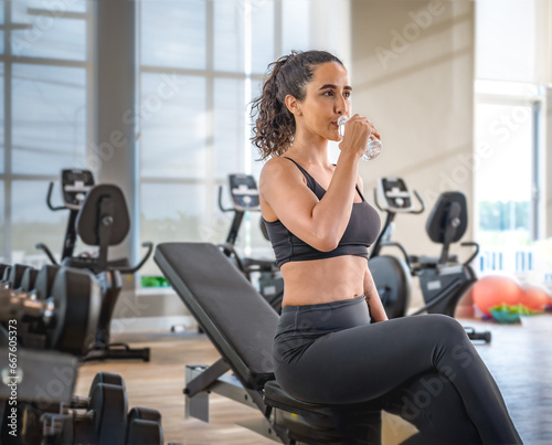 Exhausted woman in sportswear sitting at fitness training in .sporty athletic woman warm up training sitting near treadmill look aside in gym indoor Workout sport motivation