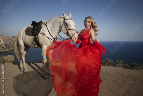 Cheerful bright girl leans on the horse, eyes closed, hand on the hair. Fashion blonde in the red dress. photo