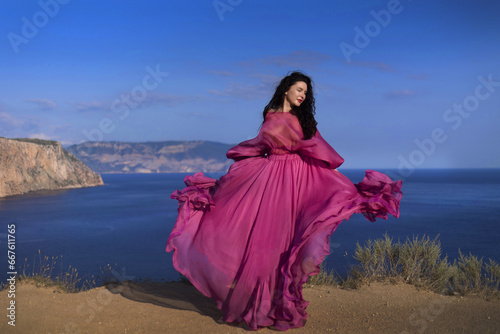 Beautiful girl in a long pink dress standing on the edge of the white cliffs