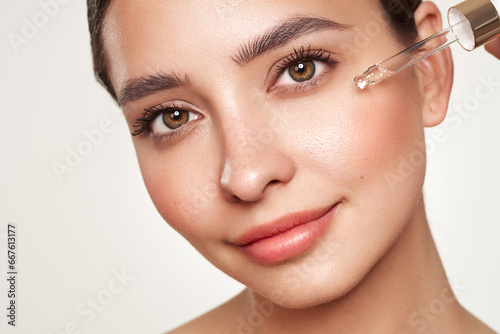 Young beautiful woman applying face serum with pipette. Cosmetic procedures for facial skin care photo