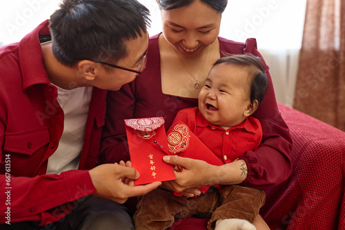 Portrait of happy Asian family with cute baby boy enjoying Chinese New Year celebration at home and holding red envelopes Have overflowing abundance every year