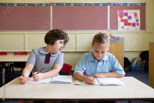 Two young girls sitting working in a primary school classroom together