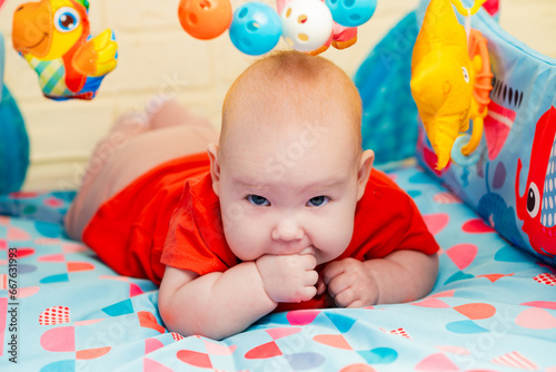 A close-up portrait of a cute adorable newborn baby with blue eyes licking his sucking fingers with a fist. The child is teething.