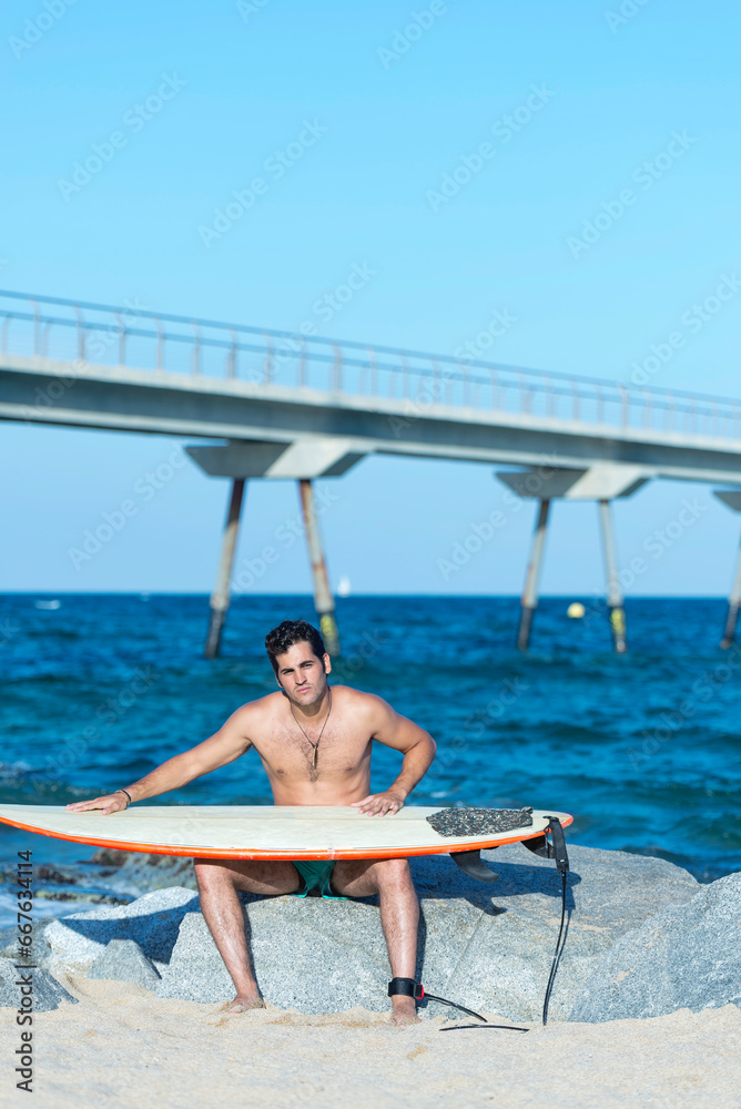 Serious young man cleaning surfboard on sunny beach