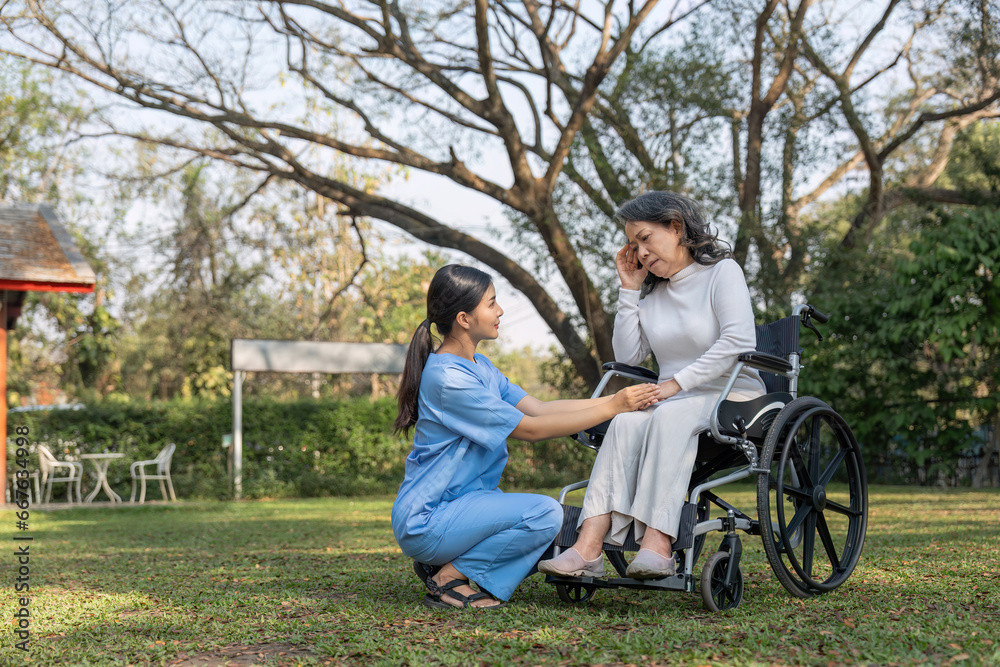Young asian care helper with asia elderly woman on wheelchair relax together park outdoors to help and encourage and rest your mind with green nature. hold hands to encourage Young asian care helper with asia elderly woman on wheelchair relax together park outdoors to help and encourage and rest your mind with green nature. hold hands to encourage