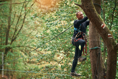 Process of preparing. Man is doing climbing in the forest by use of safety equipment © standret