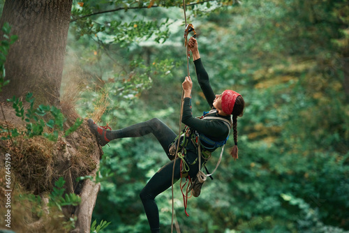 View from the side, hanging on the rope. Woman is doing climbing in the forest by the use of safety equipment