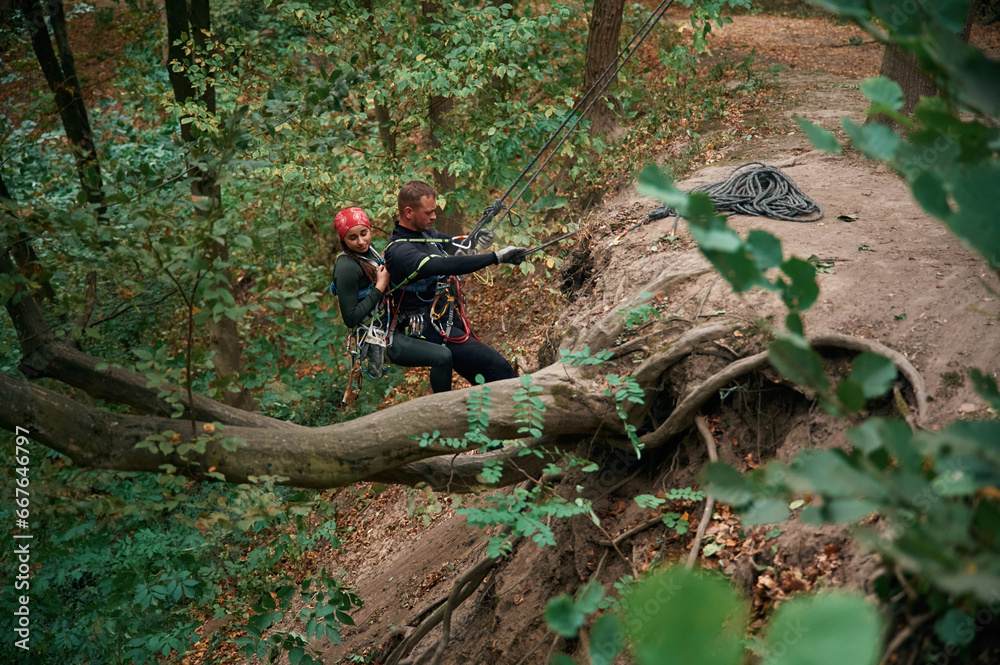 Going down. Man and woman doing climbing in forest with use of safety equipment Going down. Man and woman doing climbing in forest with use of safety equipment