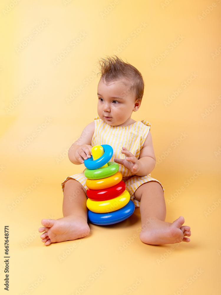 For nine months, the baby plays with a colored pyramid on a yolk background. Emotions, beautiful child. For nine months, the baby plays with a colored pyramid on a yolk background. Emotions, beautiful child.