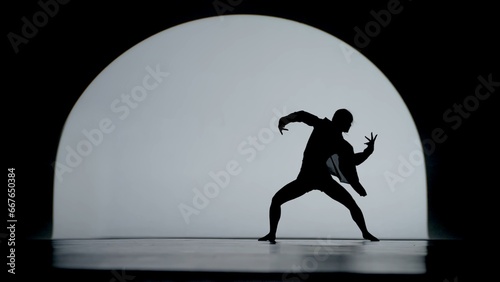 Contrasting silhouette of a young woman performing contemporary dance in the studio. Female figure dancing under a spotlight. Full size.