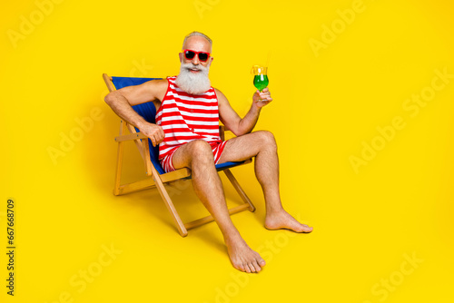 Full body photo of handsome cheerful person chill lounger hold drink glass empty space isolated on yellow color background