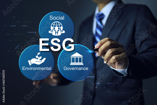 Businessman writing a pen on ESG environmental social governance icon to applied standards and environment action to regulation requirement for complied with business activity