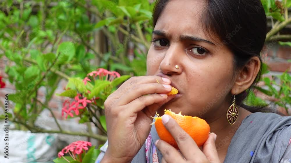 Happy young woman sitting in the garden eating orange fruit. Beautiful Asian young woman eating fresh citrus fruit outdoors. Healthy fresh food and vegetarian dieting ideas. 4k video. Happy young woman sitting in the garden eating orange fruit. Beautiful Asian young woman eating fresh citrus fruit outdoors. Healthy fresh food and vegetarian dieting ideas. 4k video.