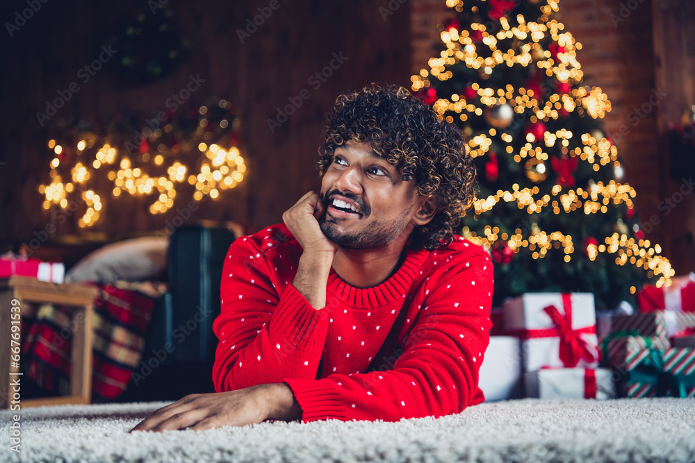 Photo of dreaming happy young arab guy touch cheek looking curious at his surprise happy new year holiday indoors fir tree background