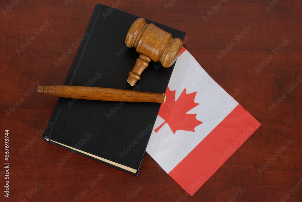 Broken gavel and legal book with flag of Canada on wooden table.