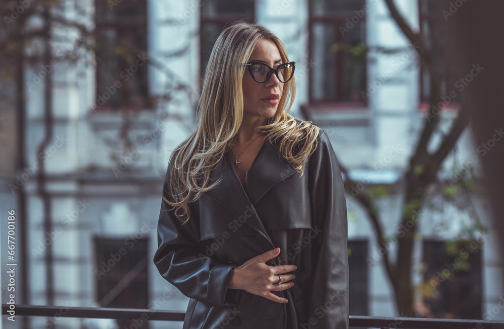 Woman in leather trench, new collection. Stylish blonde European lady at city center