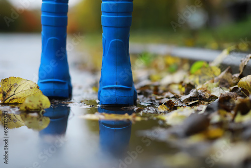 Fototapeta Naklejka Na Ścianę i Meble -  legs of child in blue rubber boots jumping in the autumn puddles