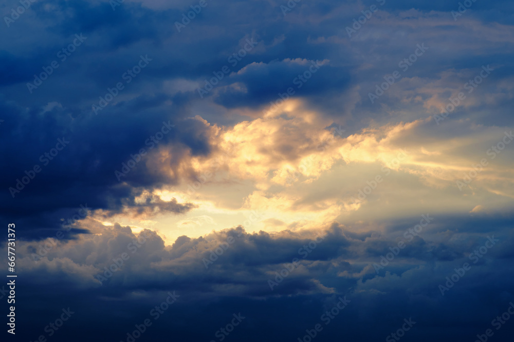 Dark storm clouds with breaking sun rays in the evening sunset sky. Dramatic sky with texture of black clouds and sunlight through the rain