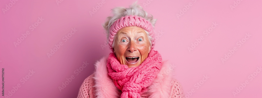 Excited eccentric elderly granny wearing knit sweater winter clothes and headband, pink background, surprised expression