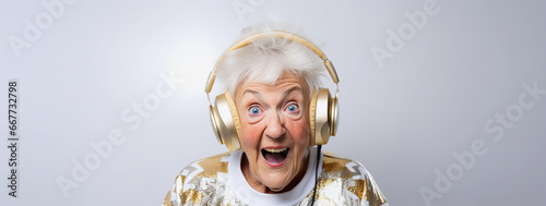 Excited elderly granny wearing gold headphones and sparkly festive holiday sweater listening to music for New Year's eve countdown celebration, amazed expression, gray background photo