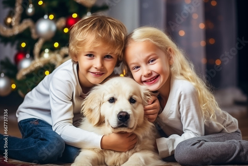 Little children and their dog at home near the Christmas tree. Small children playing with dog indoors at home at Christmas time.