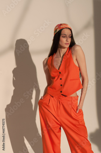 A beautiful young girl in an orange suit and bandana stands on a white background. Hard light
