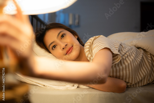Asian woman lying on the bed turning off the light at the bedside to sleep tonight.