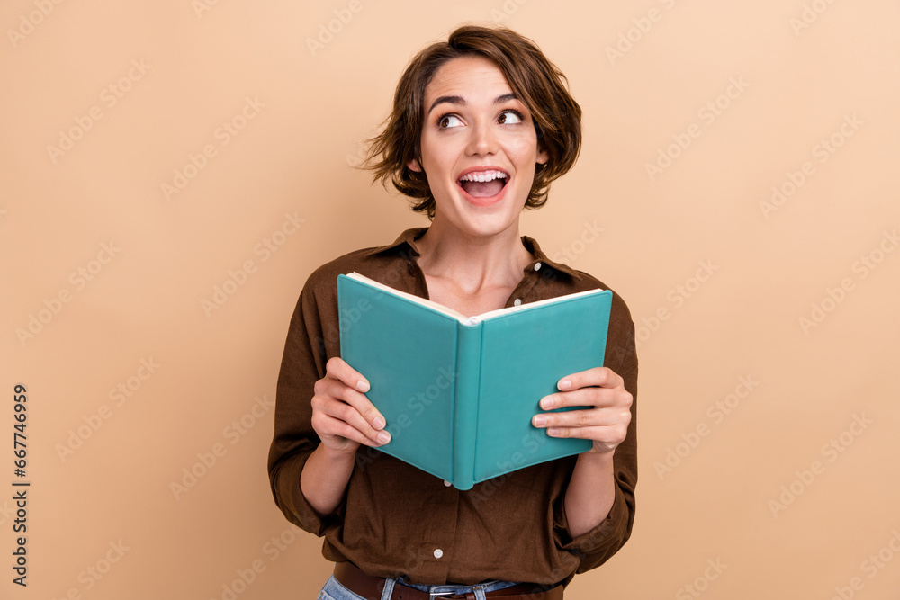 Photo of positive excited girl dressed brown shirt reading interesting book looking empty space isolated beige color background Photo of positive excited girl dressed brown shirt reading interesting book looking empty space isolated beige color background